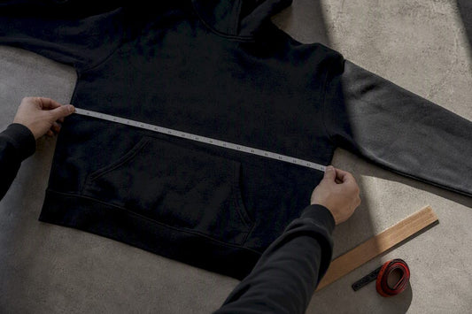 Hands measuring a flat hoodie chest